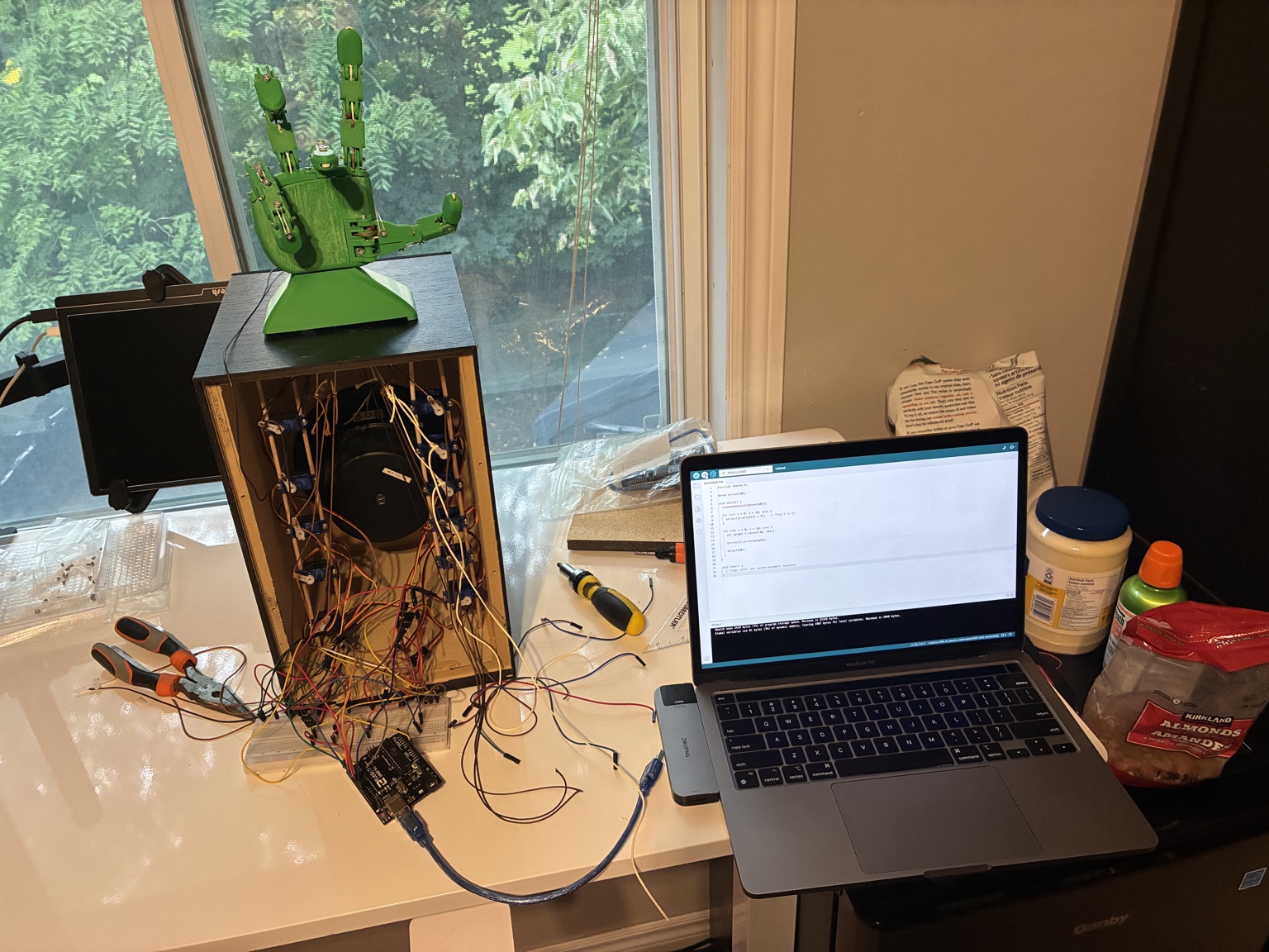 My robotic hand, exposed mechanism and wiring, tools, and laptop on the workbench